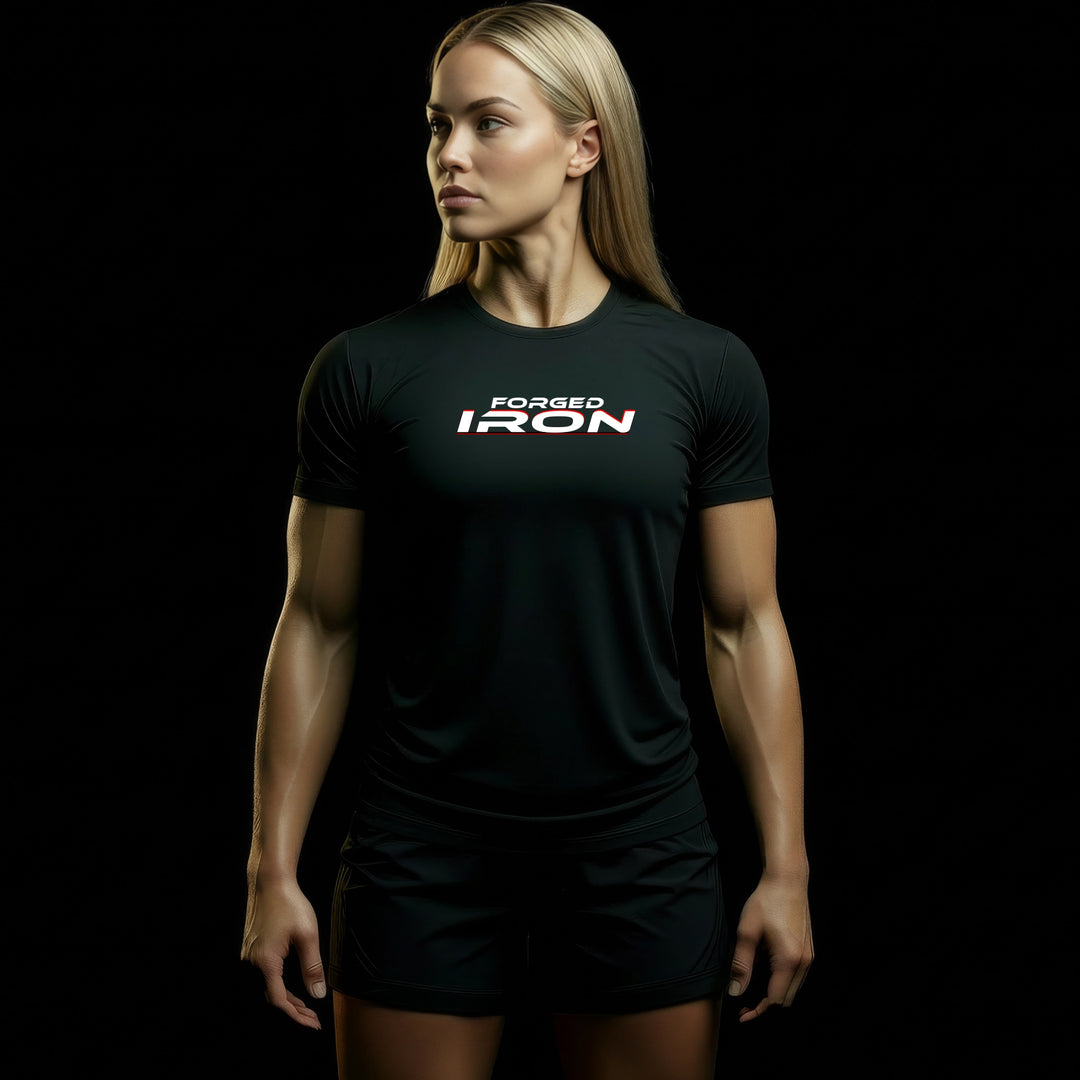 MAXPULSE™ CORE | FORGED IRON | Women Athletic Fit Tee | BlackPulse™ black performance shirt with bold FORGED IRON chest print and red accent underline | Female fitness model turned slightly to the side with strong posture in dark studio lighting | Featured in MAXPULSE™ CORE Women Tee